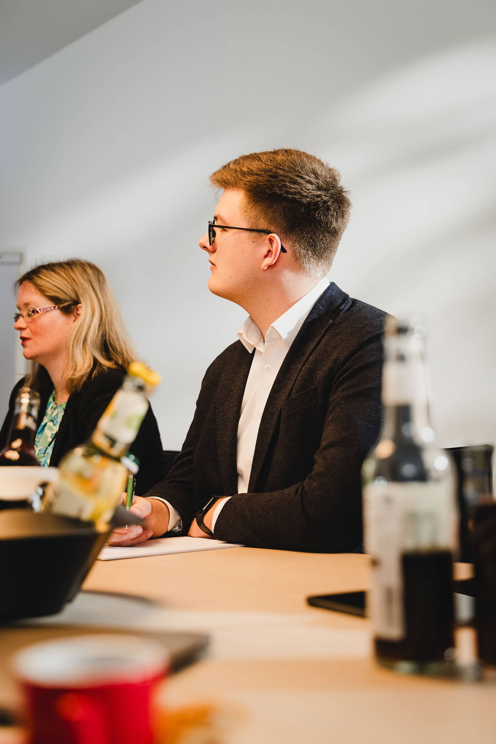 AntwortING_Stock-131 Zwei Personen in Geschäftskleidung sitzen mit Getränken und Flaschen an einem Tisch und scheinen an einer Besprechung oder Diskussion teilzunehmen.